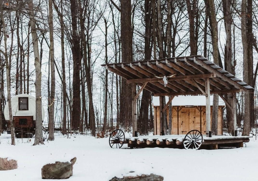 Snowy woodland with a rustic wooden shelter and wagon, bare trees in the background