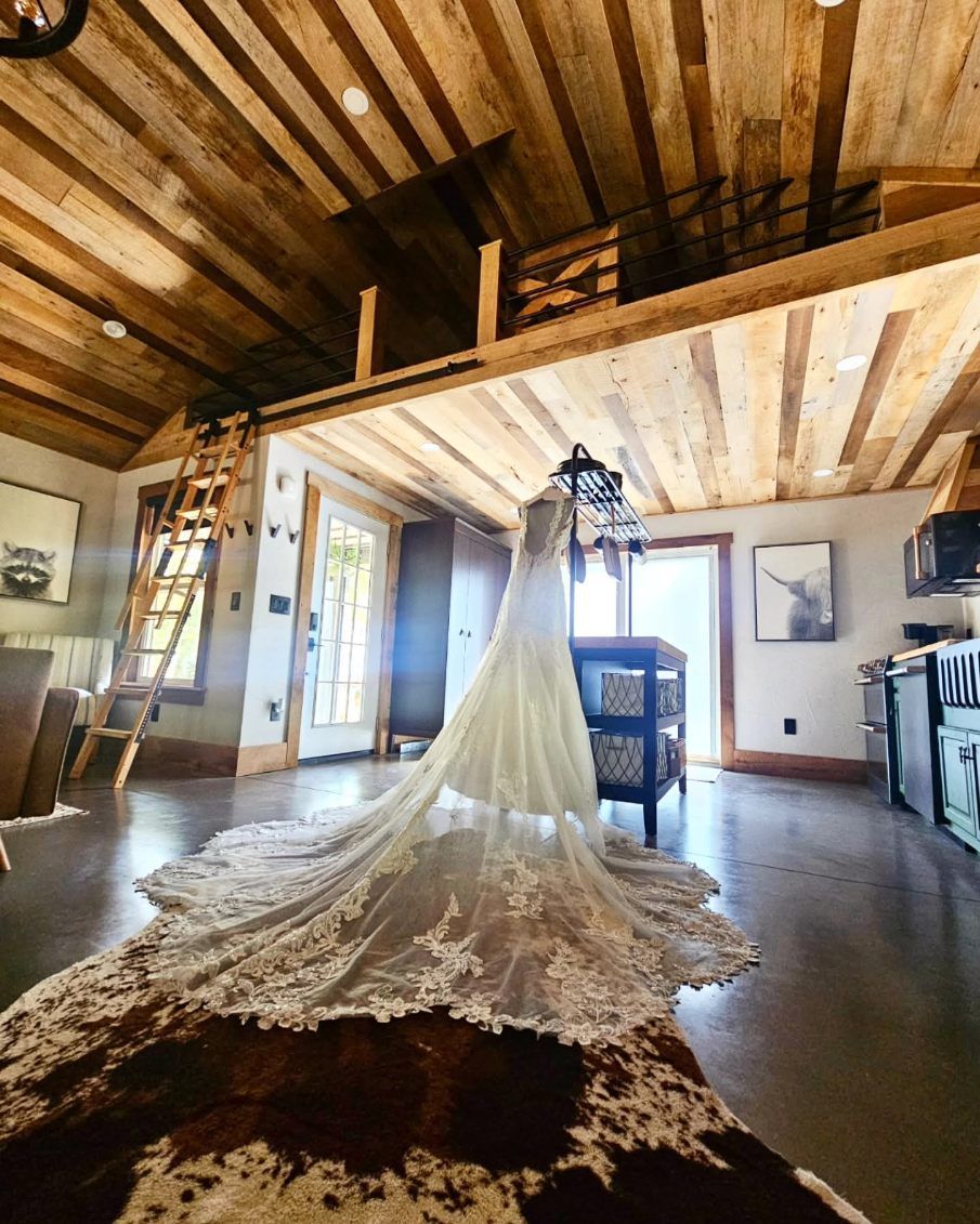 Wedding dress hanging in a rustic cabin, with a long lace train spread across the wooden floor.