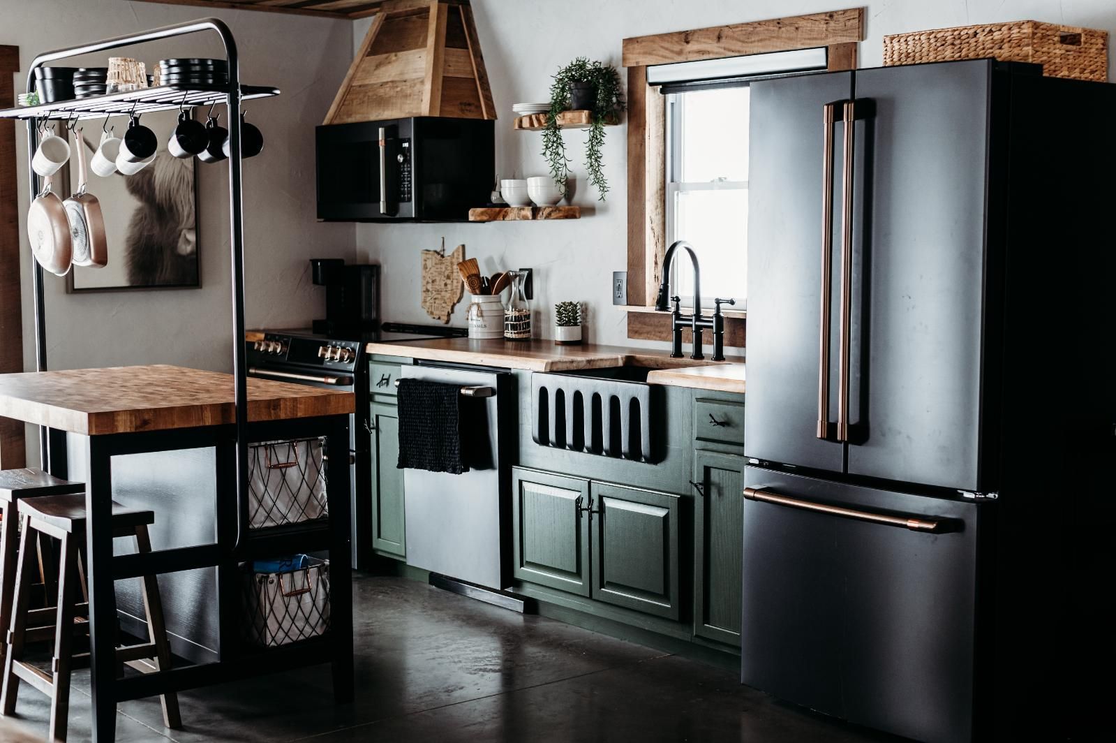 Modern kitchen with stainless steel fridge, green cabinets, wooden countertops, and hanging cookware