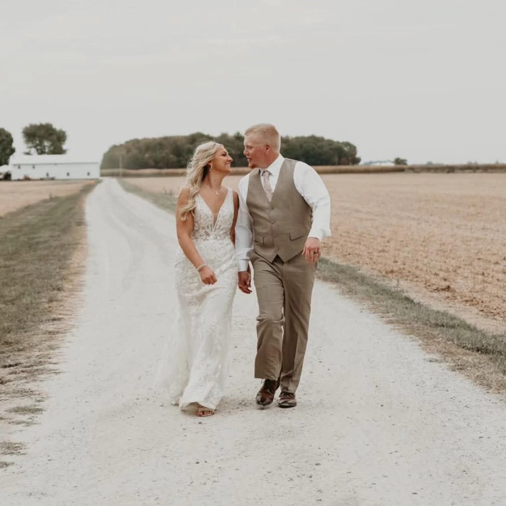 Bride and groom walking hand in hand down a gravel road in a rural field