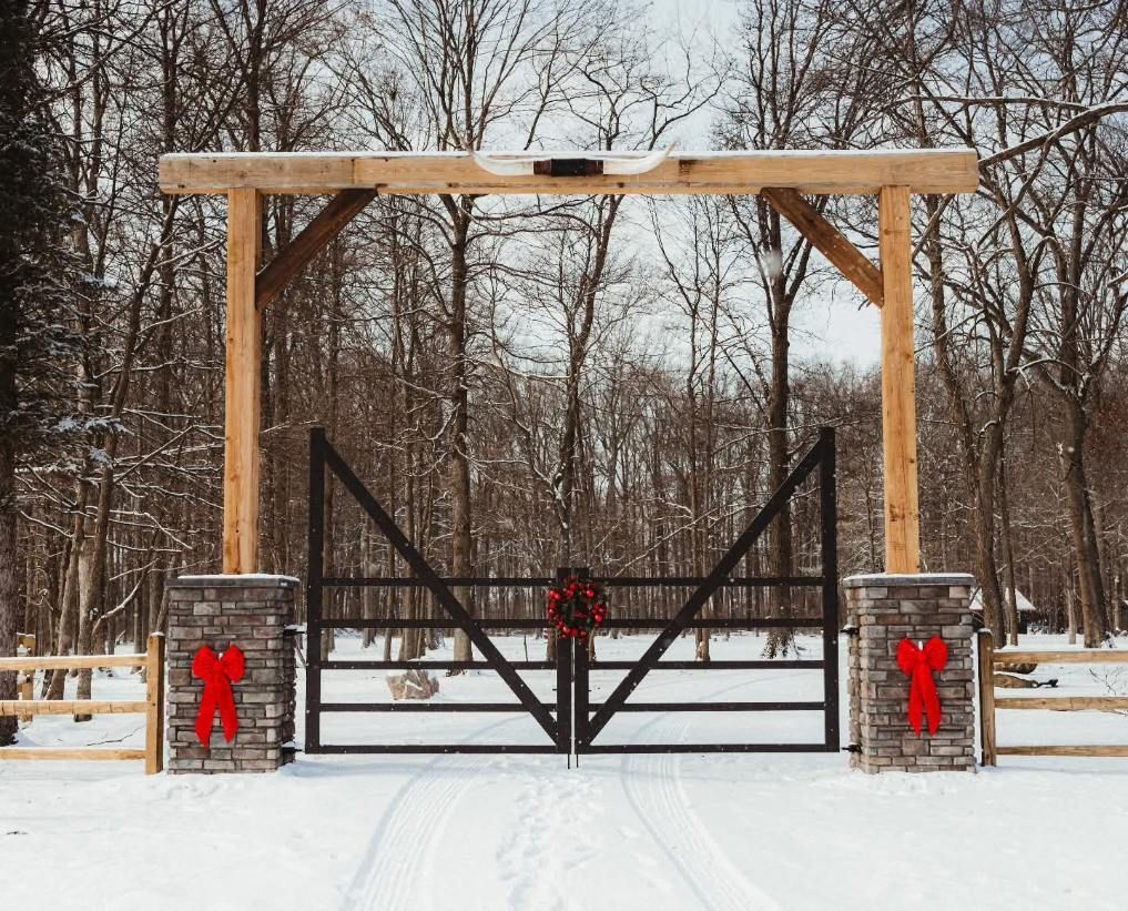 Snowy wooden gate with stone pillars and red bows in a winter forest setting