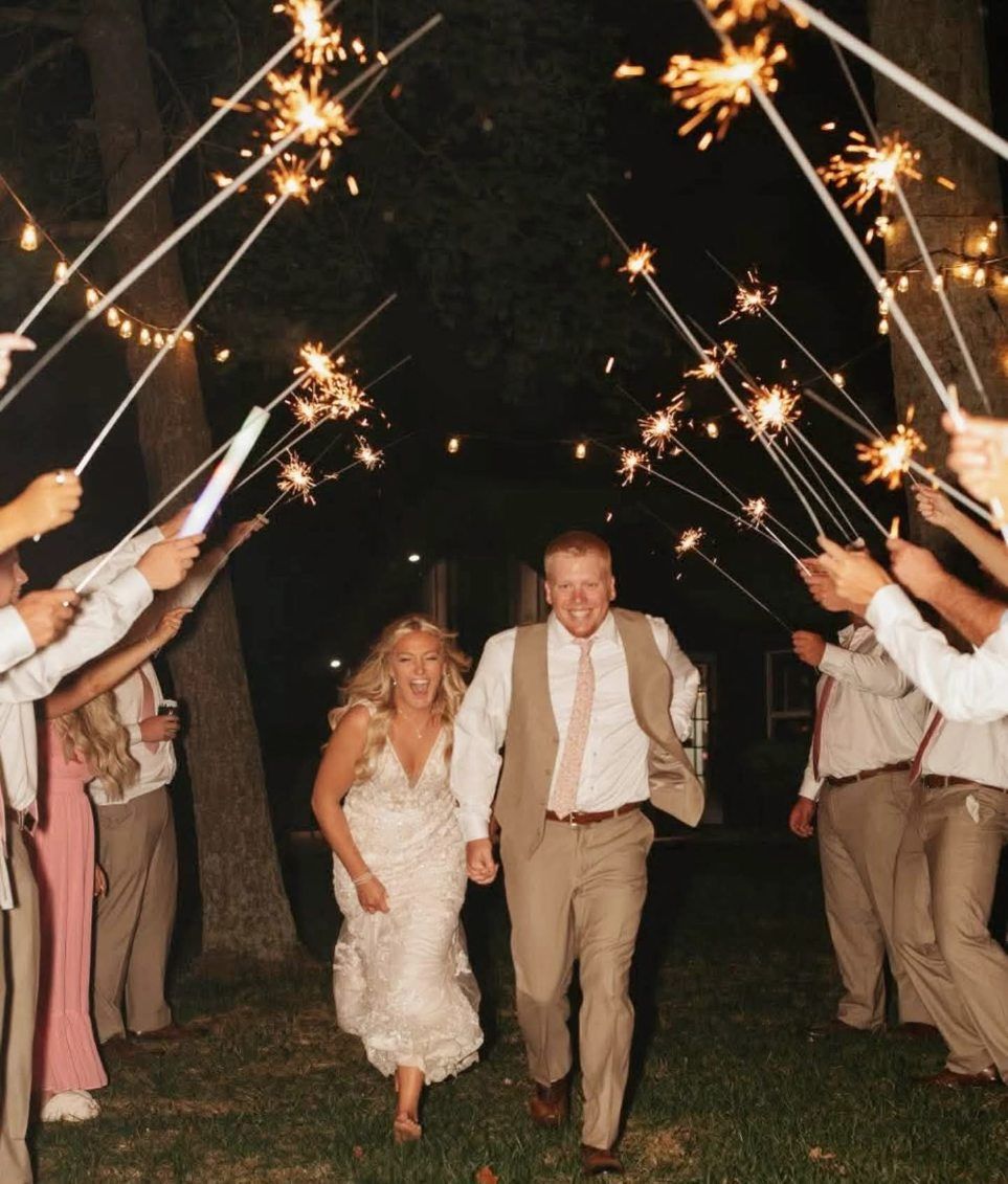 Newlyweds walking under a sparkler tunnel at night, holding hands and smiling