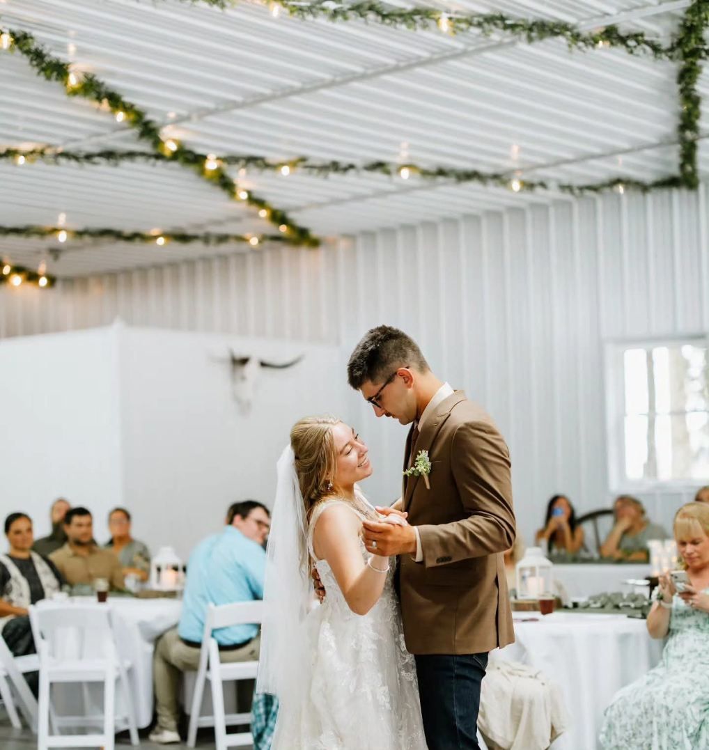 Newlyweds dancing at a decorated indoor reception with string lights and seated guests