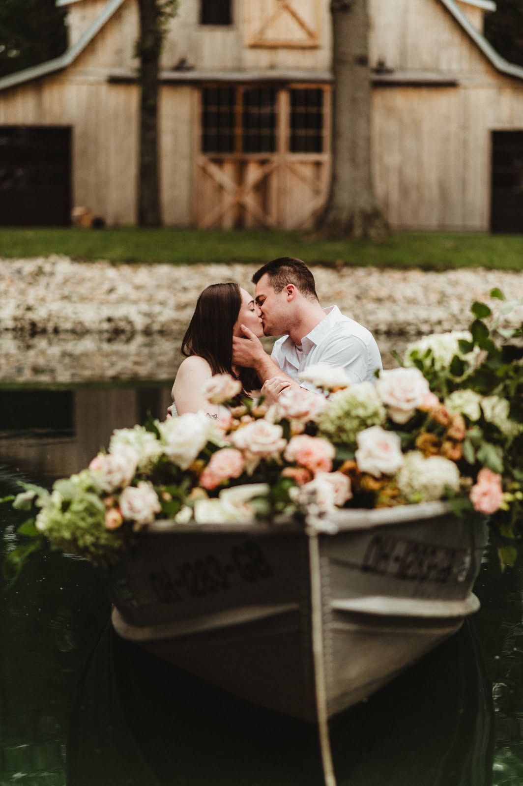 Couple kissing in a flower-filled boat before a rustic barn backdrop