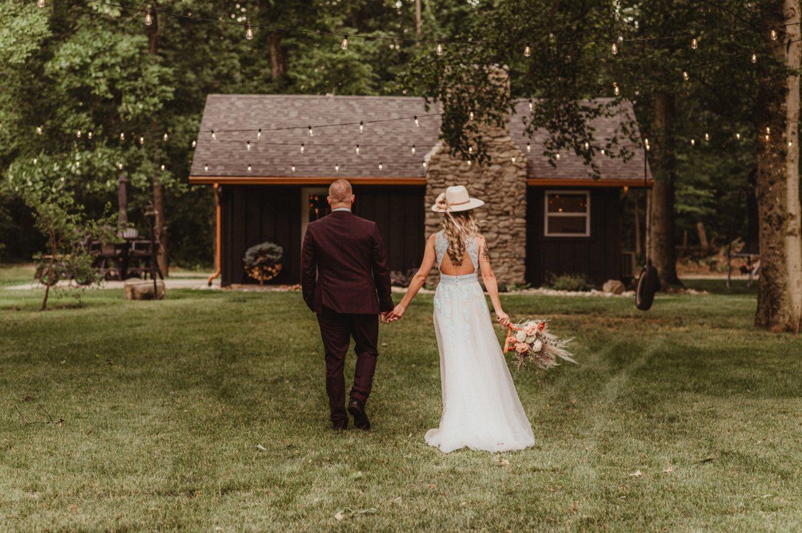 Bride and groom walking toward a rustic cabin in a wooded clearing