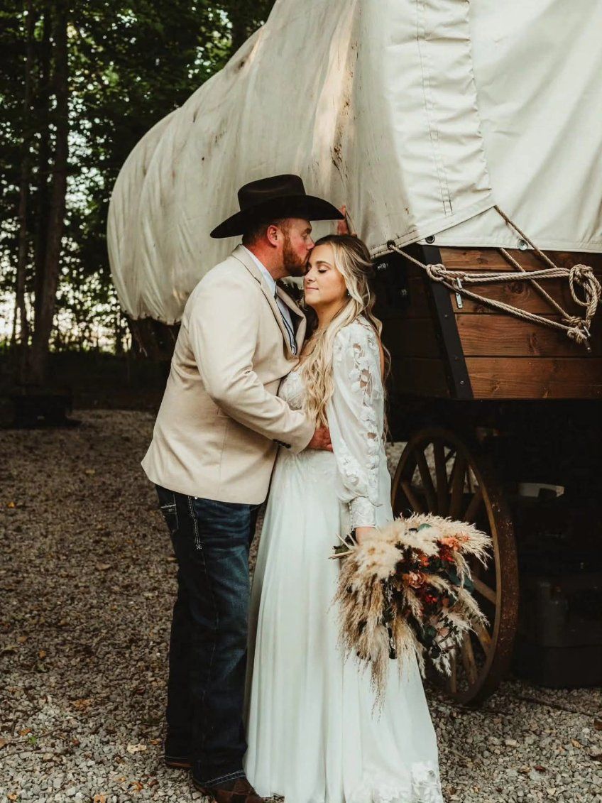 Couple embracing beside a covered wagon in a wooded outdoor setting