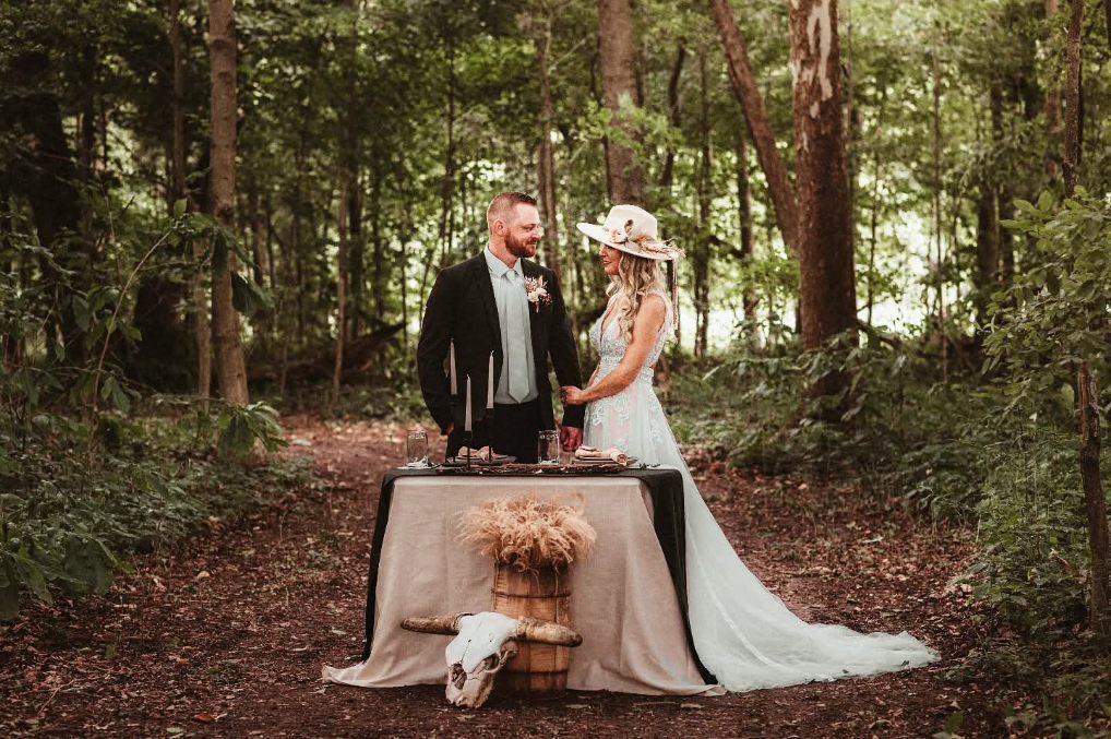 Couple exchanging vows at a rustic table in a wooded forest setting