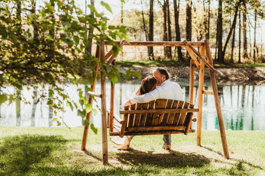 Couple sitting on a wooden swing by a calm lakeside under trees