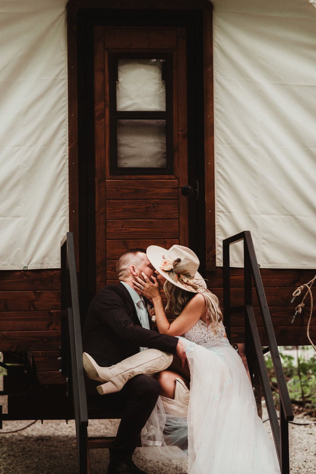 Couple in wedding attire kissing on a porch in front of a wooden cabin