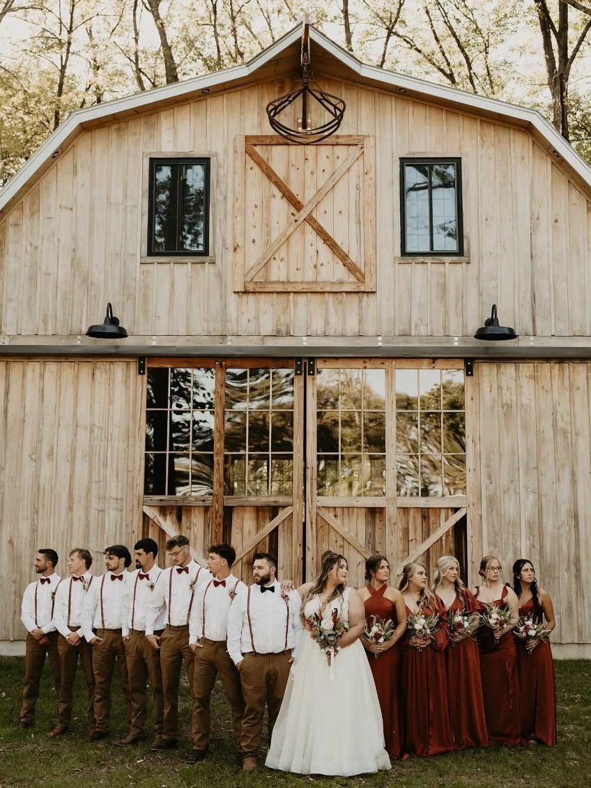 Wedding party posing in front of a rustic barn, with bridesmaids, groomsmen, and the bride in white.