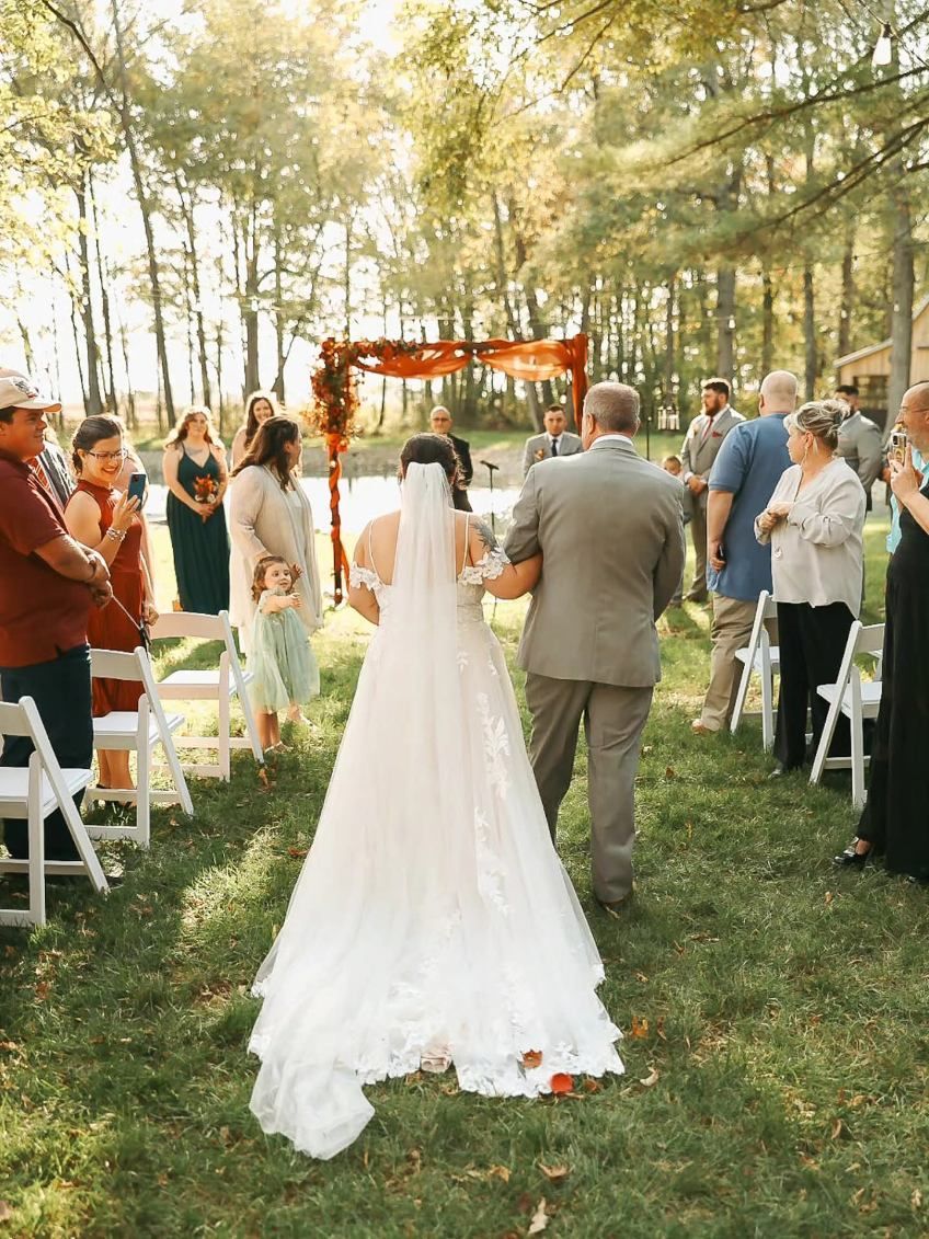 Bride and groom walking down a tree-lined aisle at an outdoor wedding ceremony