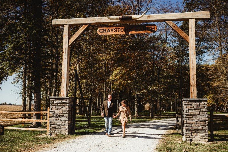 Two people walking under a wooden entrance arch in a wooded park.