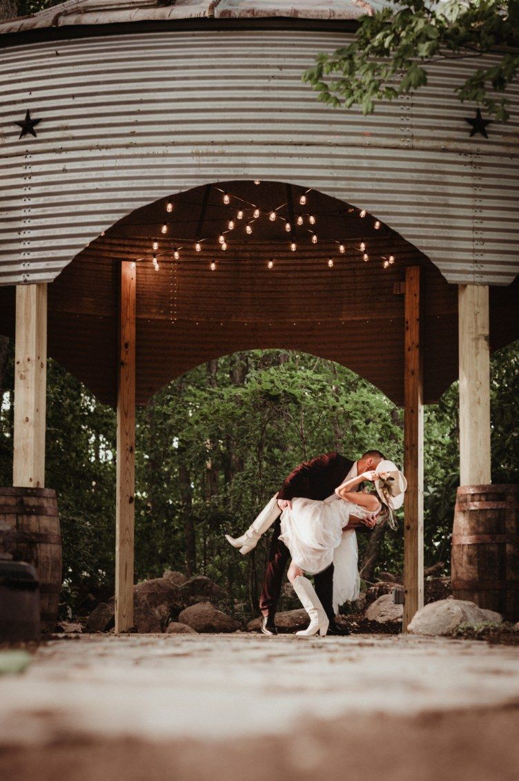 Two people dancing under a wooden archway with hanging string lights outdoors