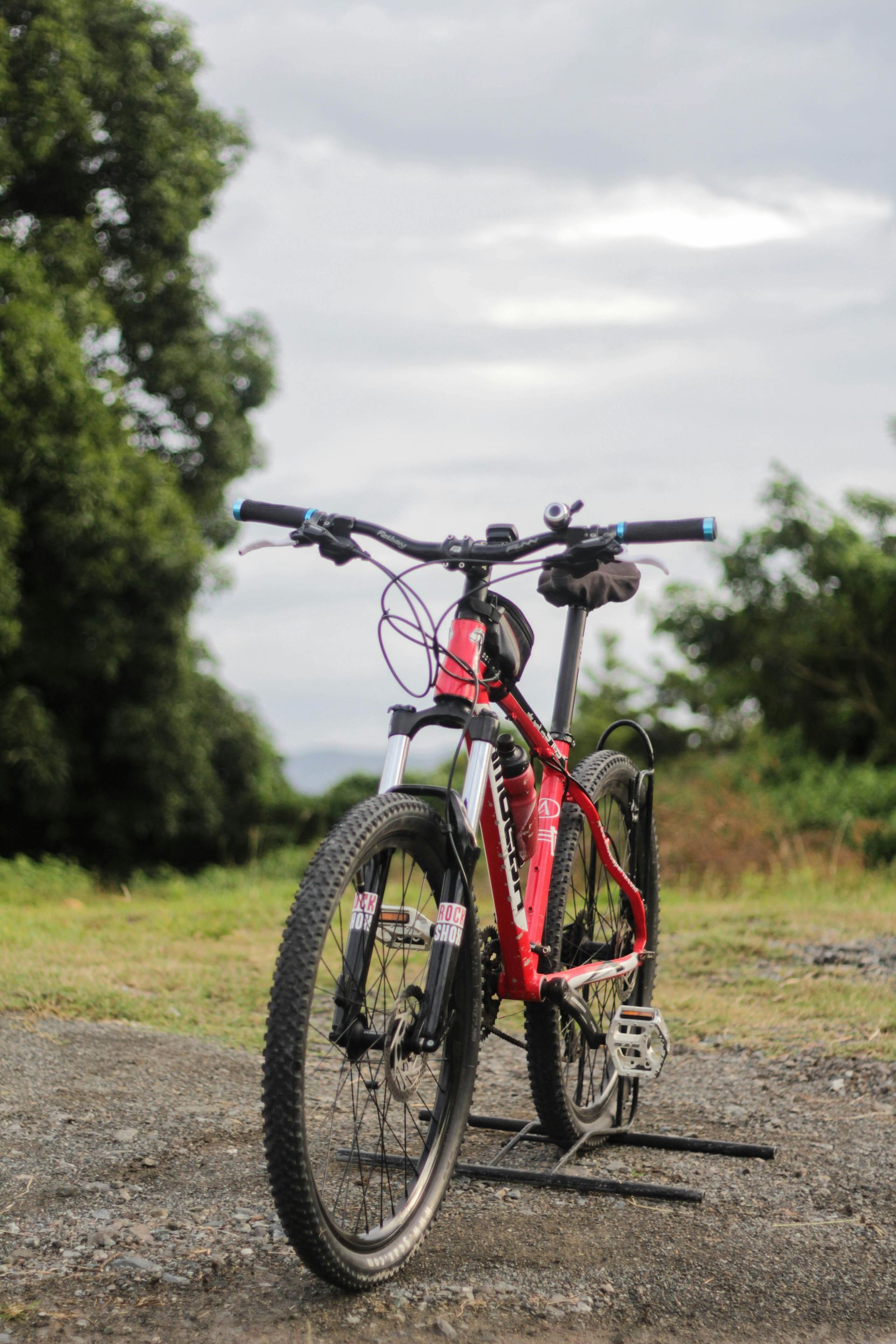 A red bicycle is parked on the side of a dirt road.