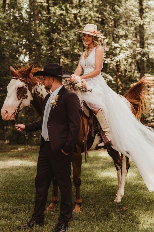 A bride and groom are posing for a picture while the bride is riding a horse.