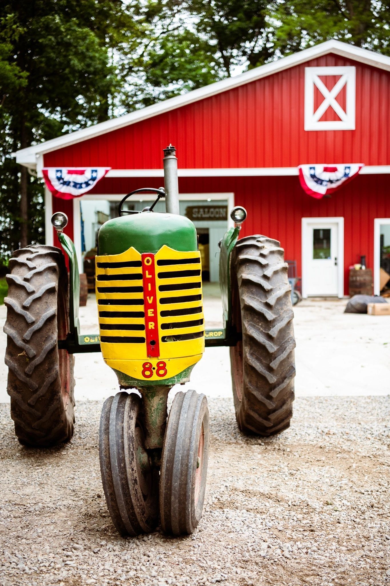 A green and yellow tractor is parked in front of a red barn.