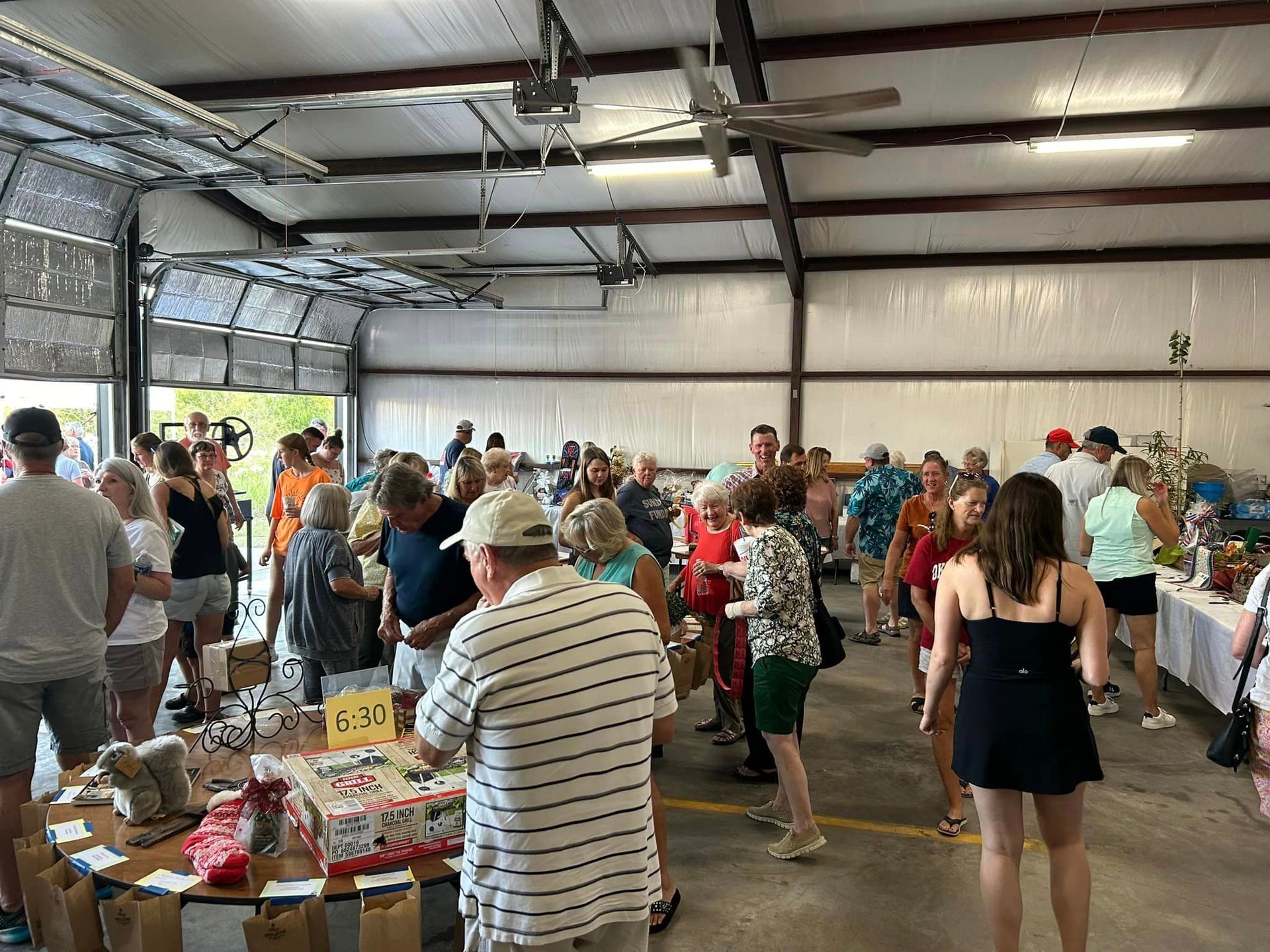 A large group of people are standing around tables in a garage.