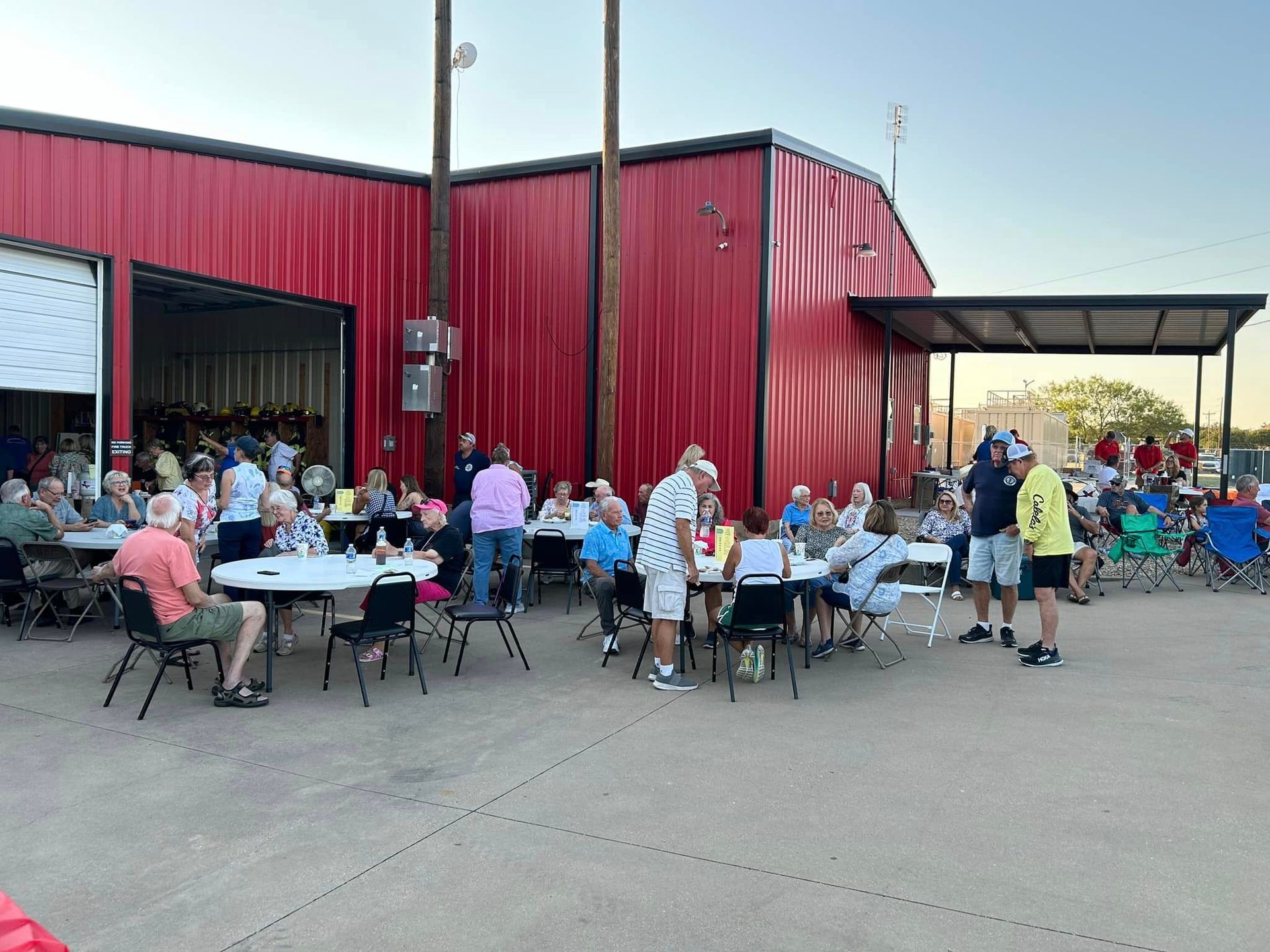 A group of people are sitting at tables outside of a red building.