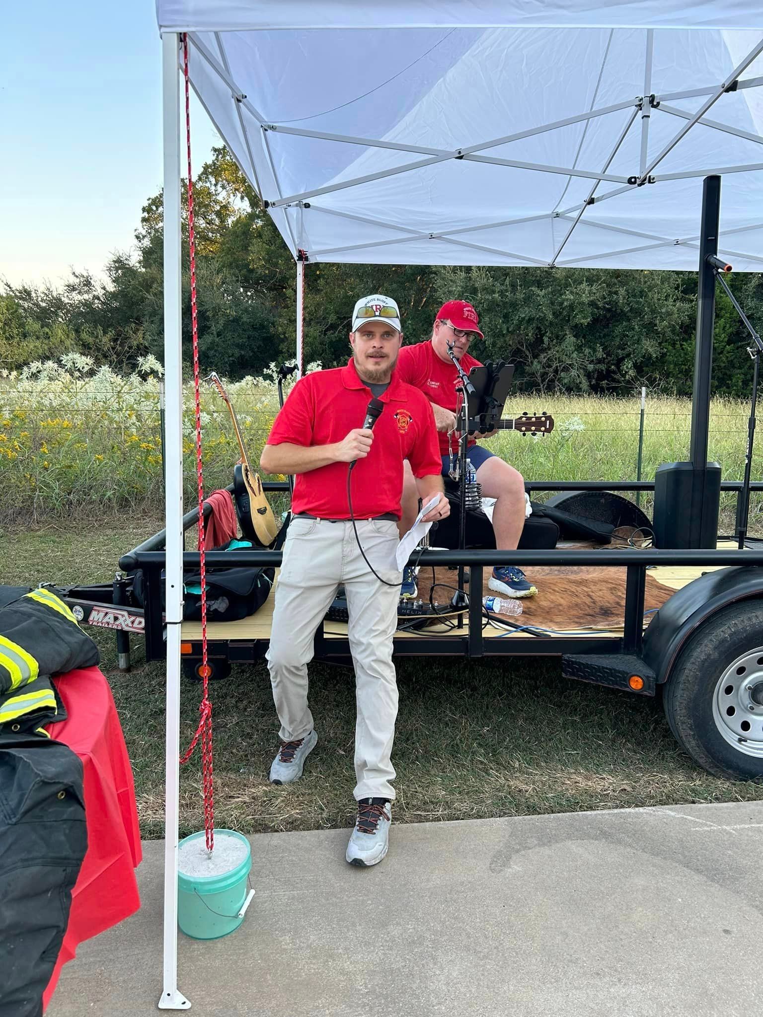 Two men are standing next to a trailer under a tent.