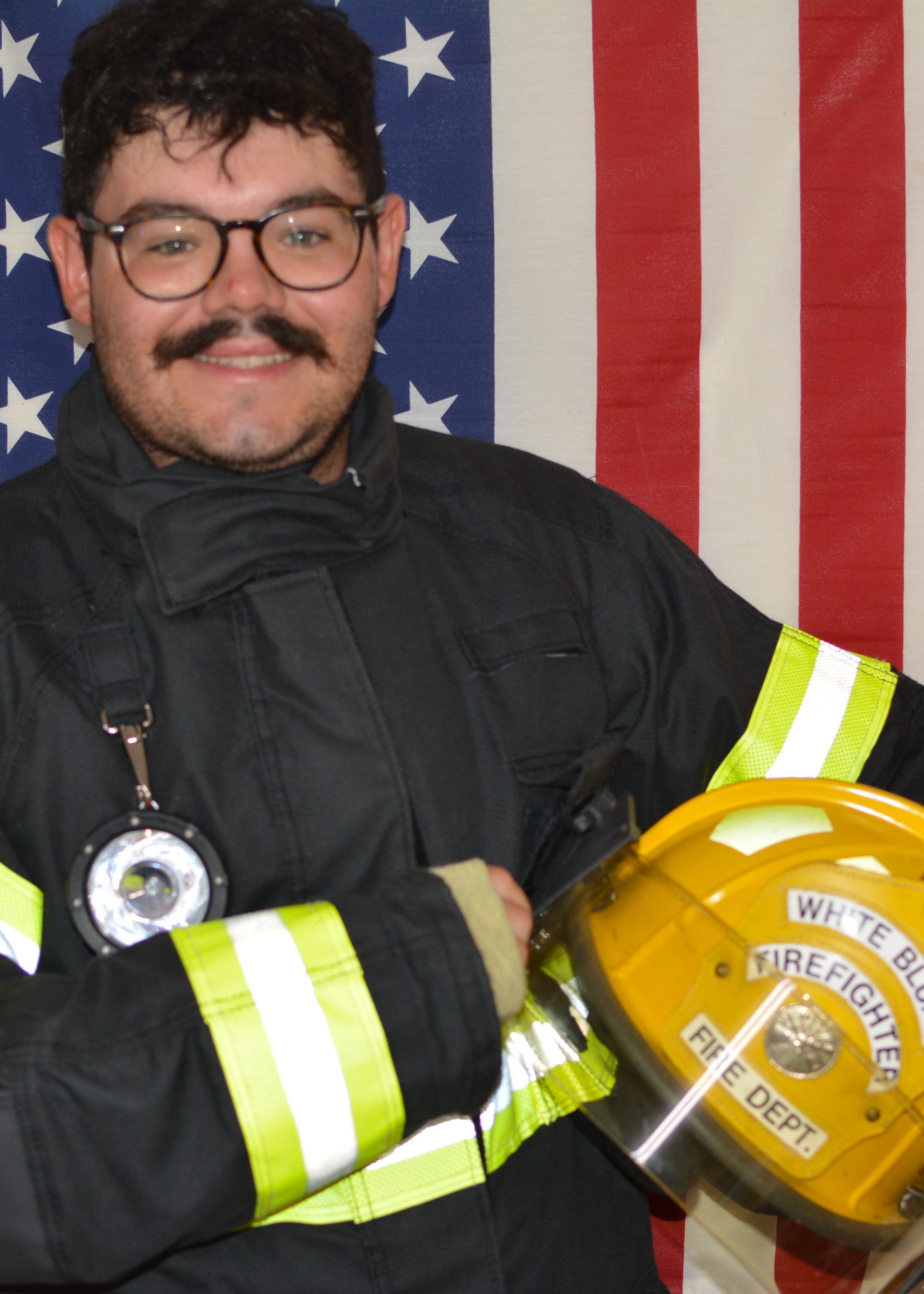 A man in a fire department uniform holds a helmet in front of an american flag