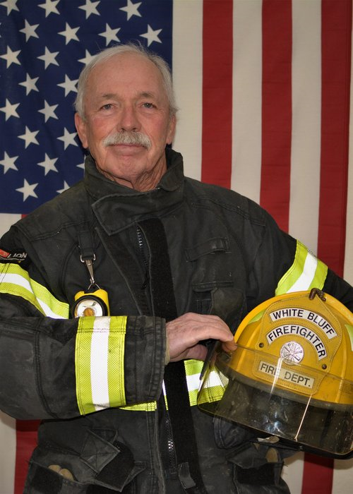 A man in a fireman 's uniform holds a helmet that says white dept