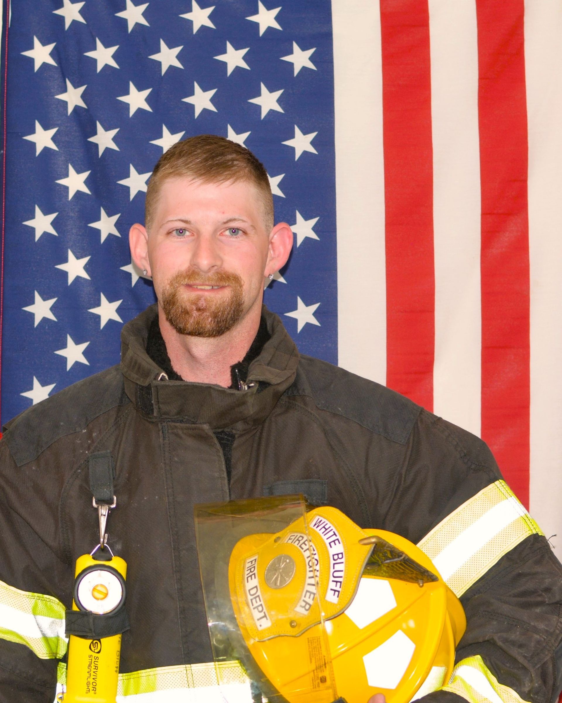 A fireman in front of an american flag holding a helmet
