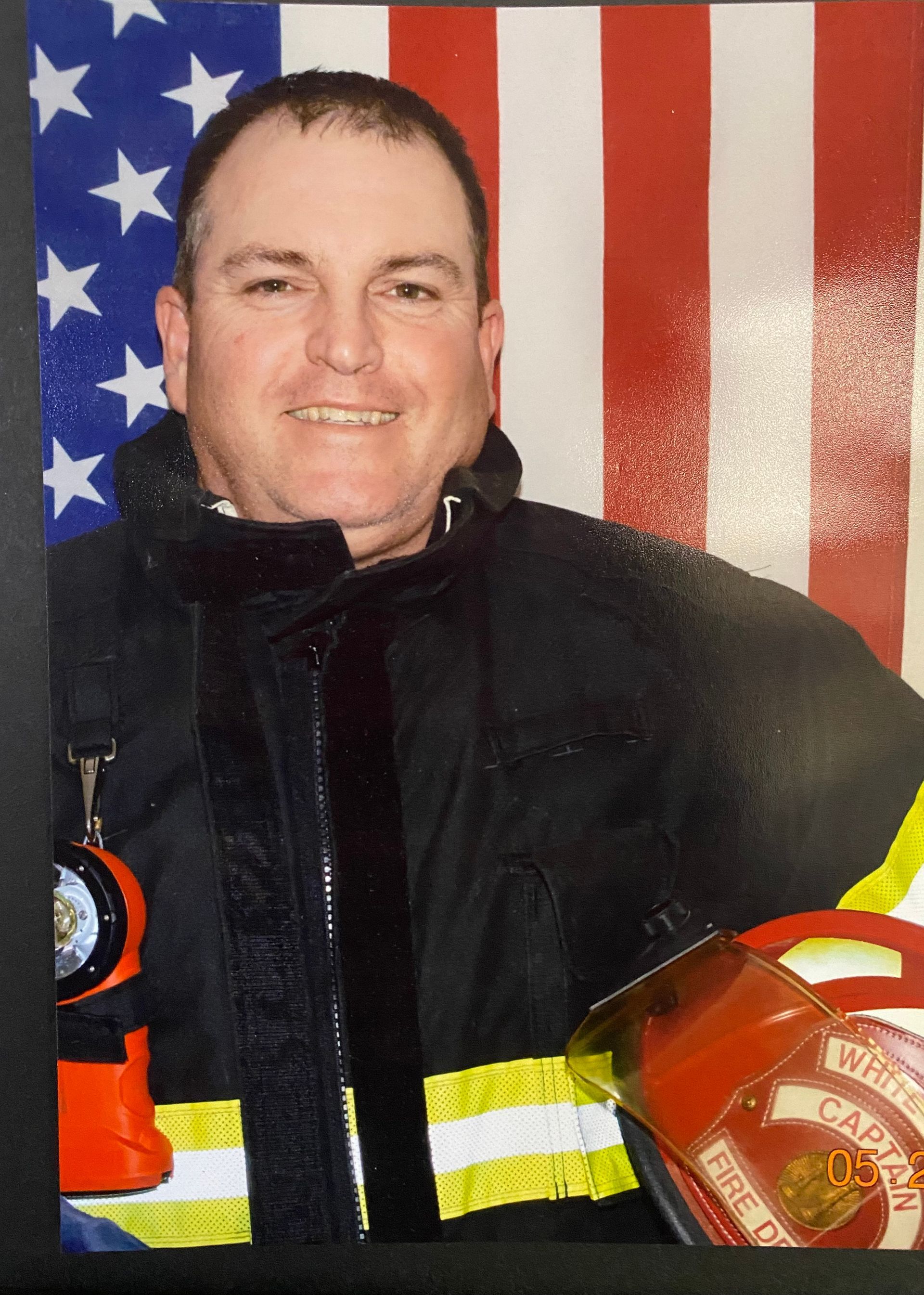 A fireman in front of an american flag holding a helmet