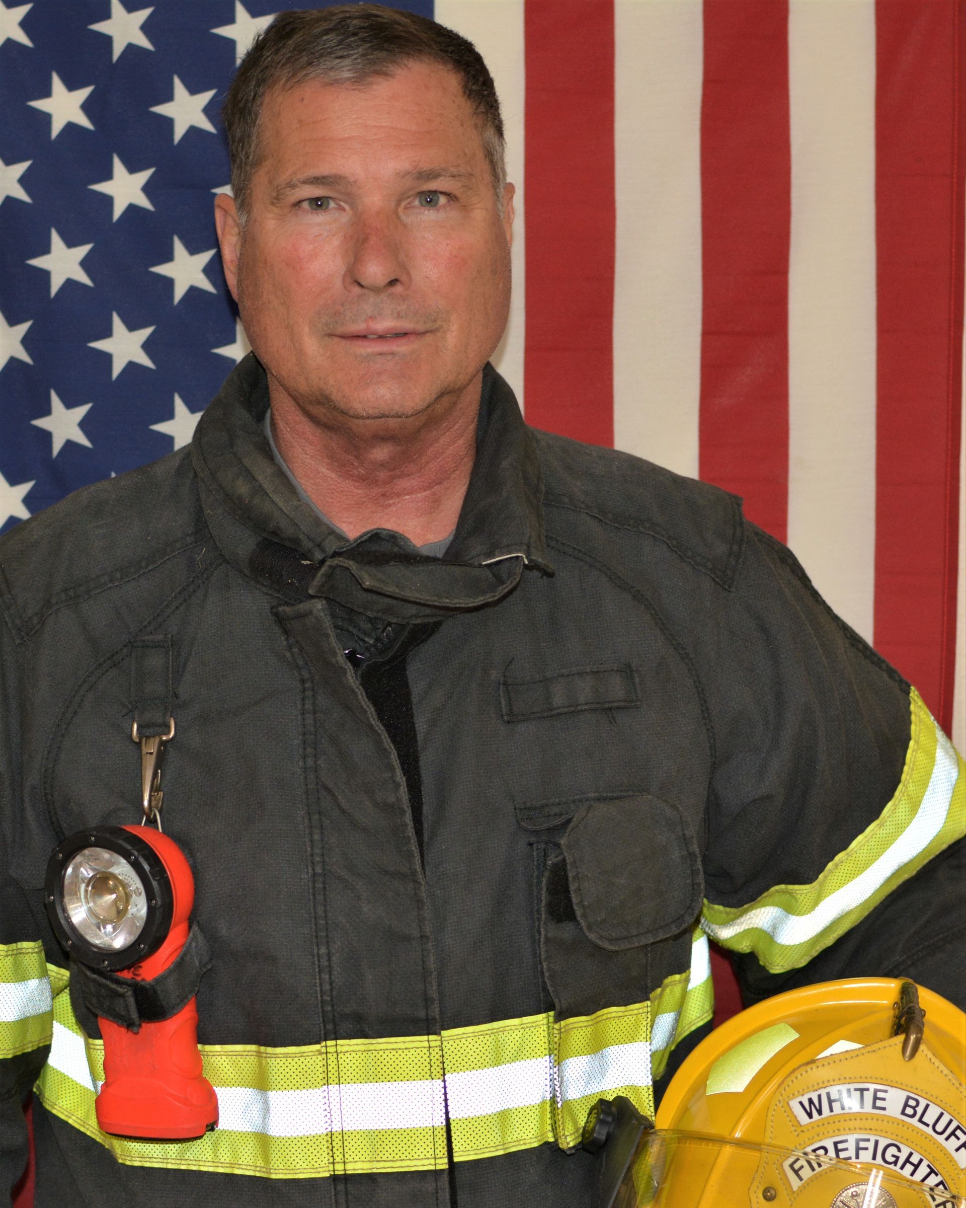 A fireman holding a helmet and a flashlight in front of an american flag