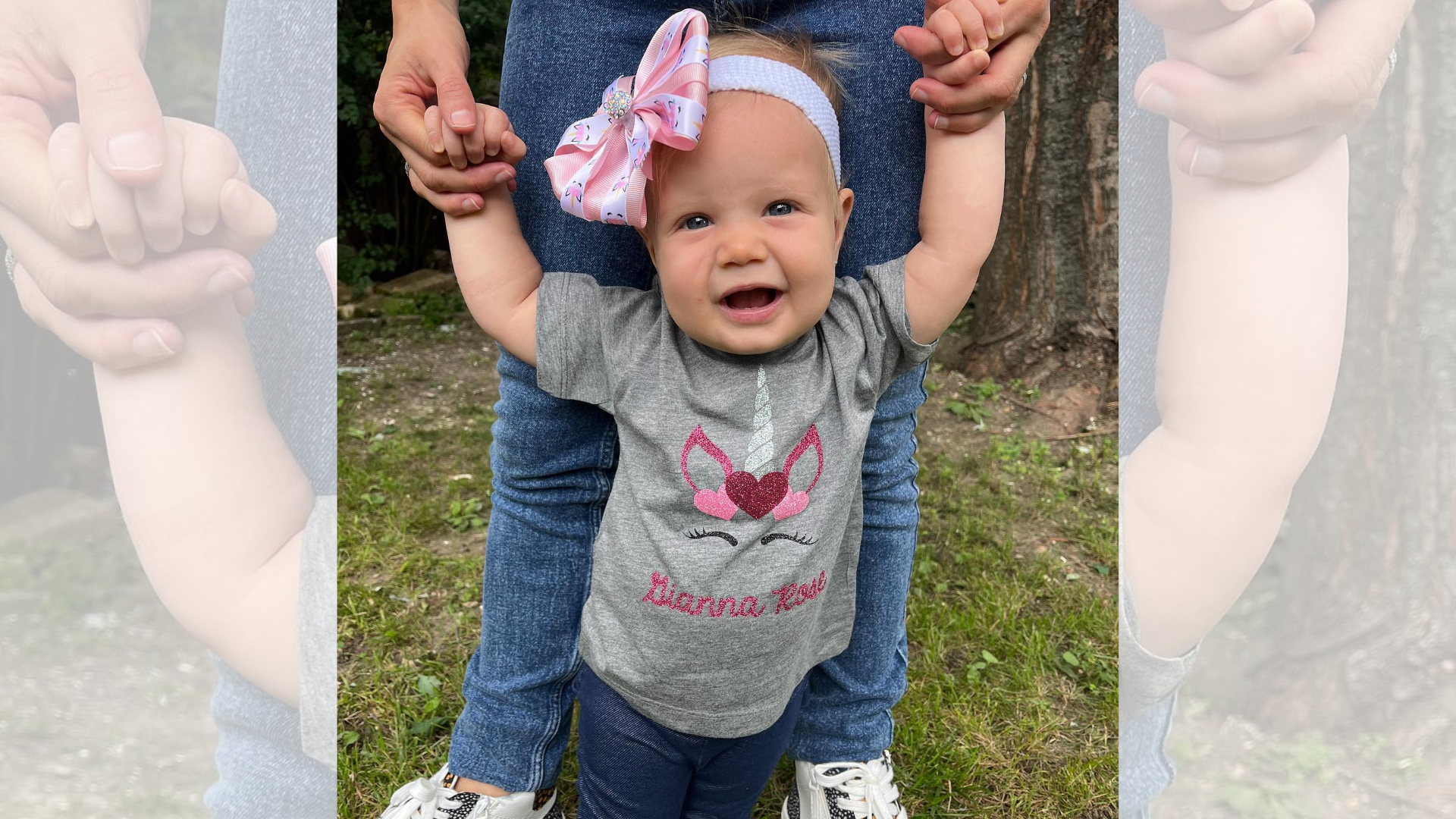 A baby girl is standing next to a woman holding her hands.