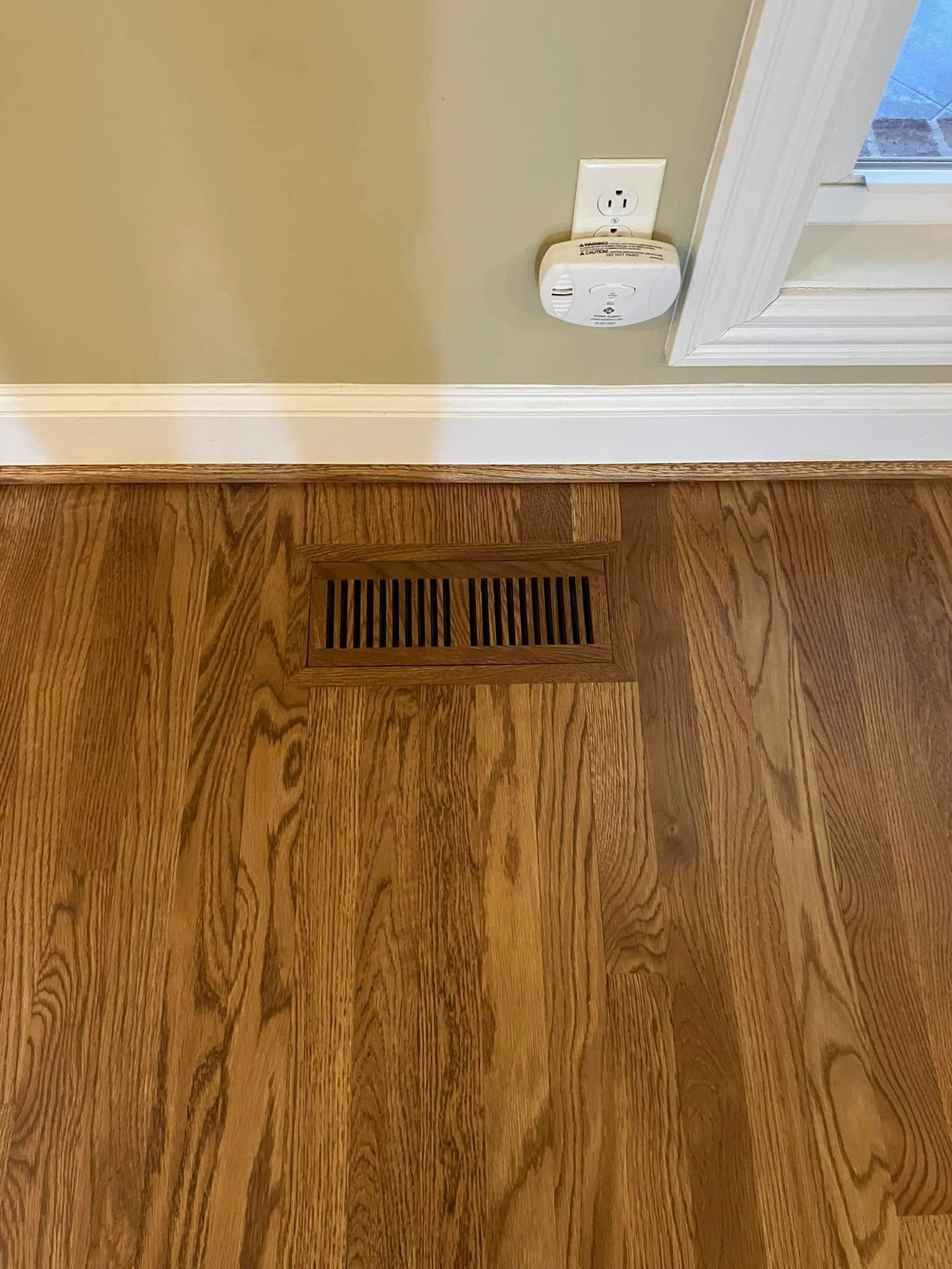 A wooden floor with a vent underneath it in a room.