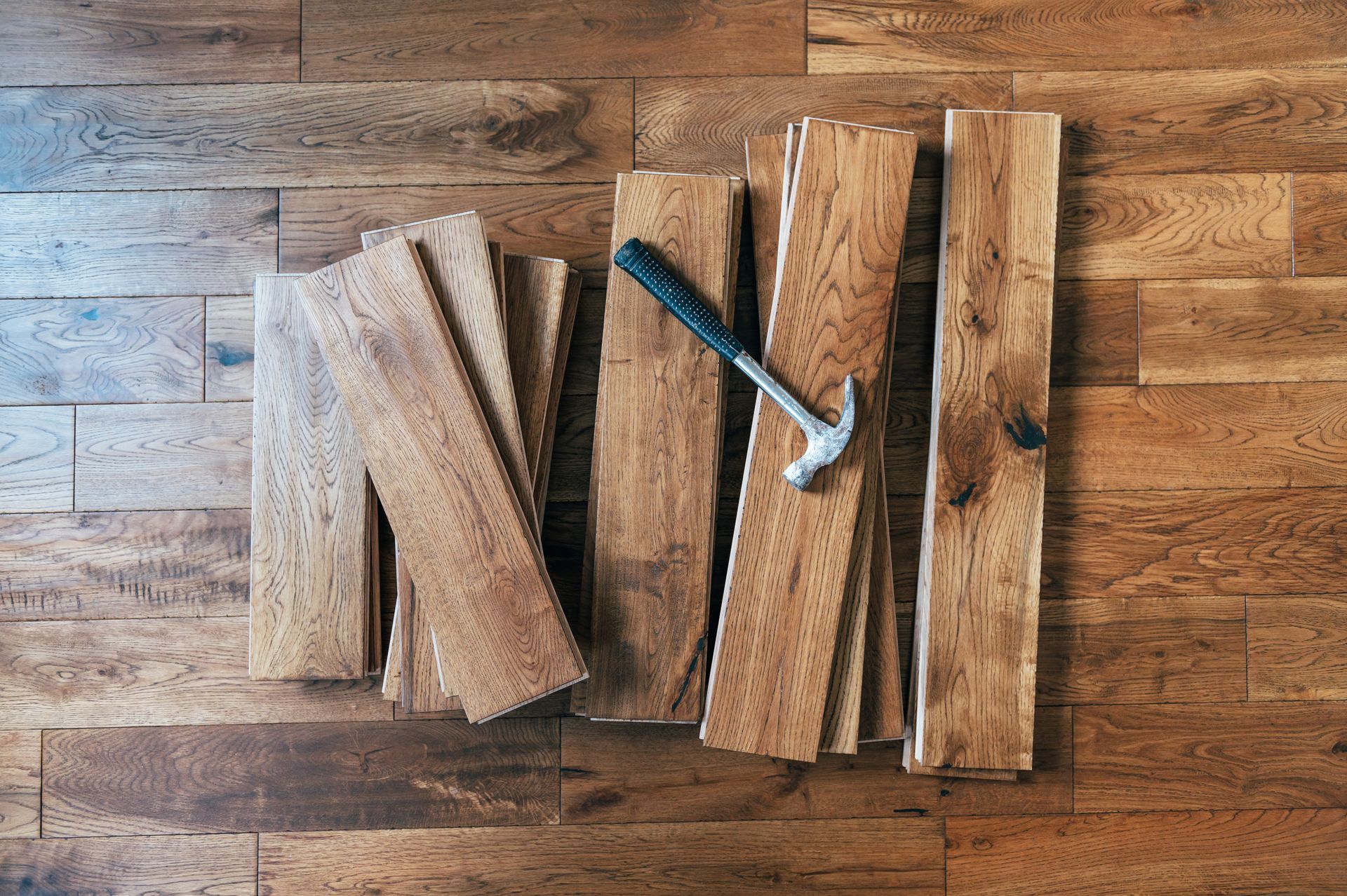 Wood flooring planks laid out on a hardwood floor with a hammer on top.
