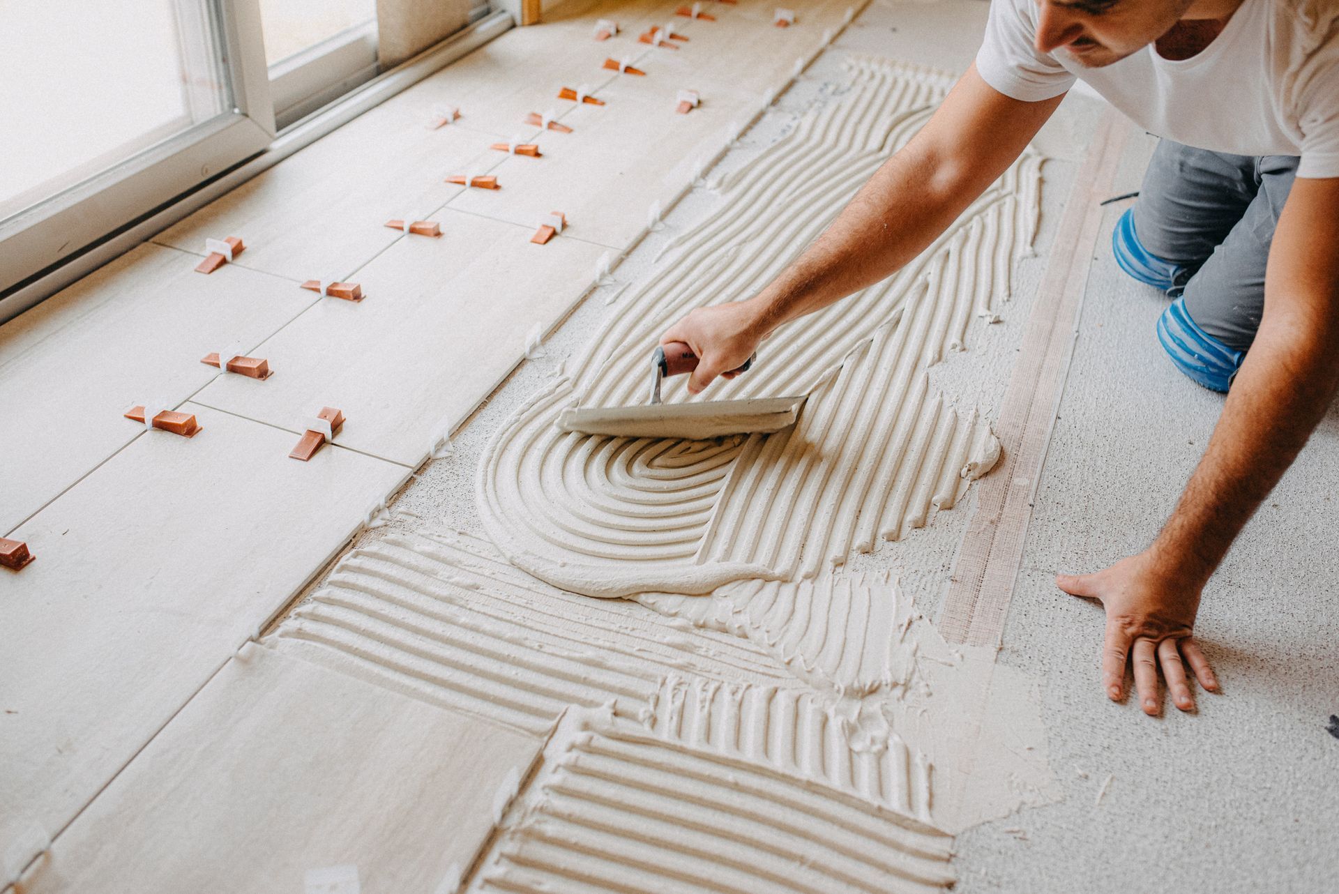 A man is laying tiles on the floor with a trowel.