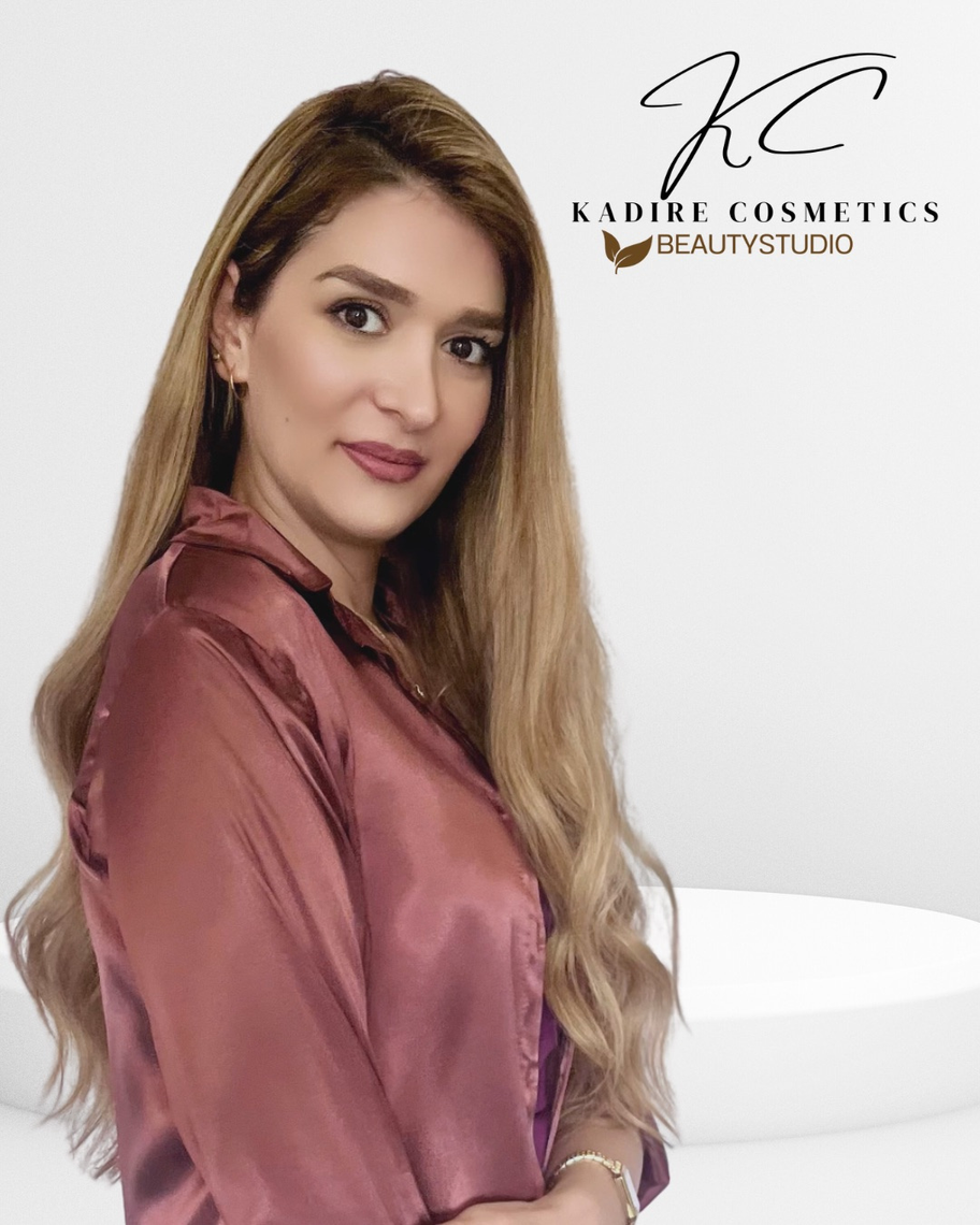 Eine Frau in einem rosa Hemd steht vor einer weißen Wand.