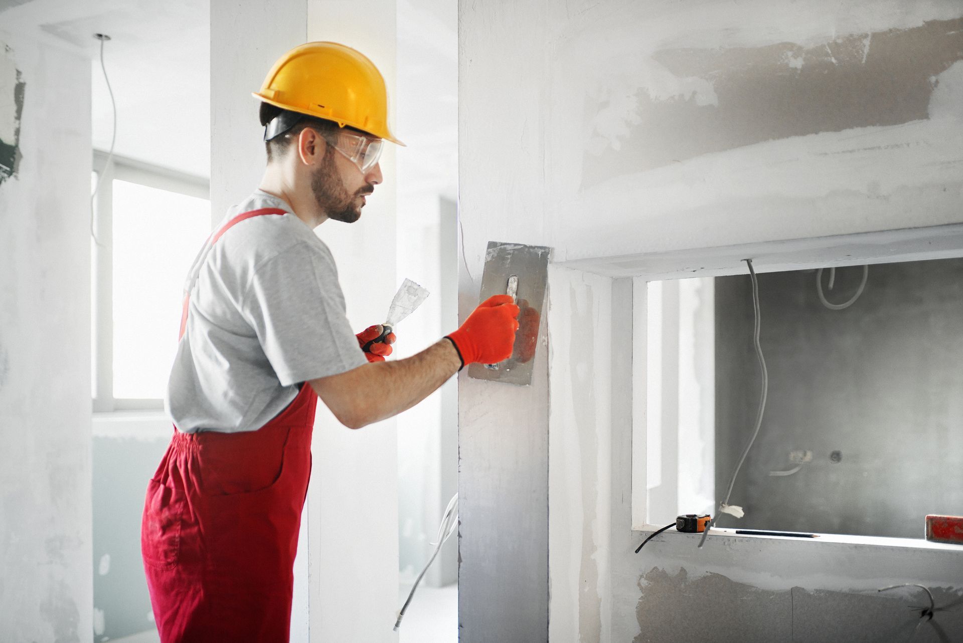 Close-up, side view of a mid-30s professional handyman applying plaster to drywall.