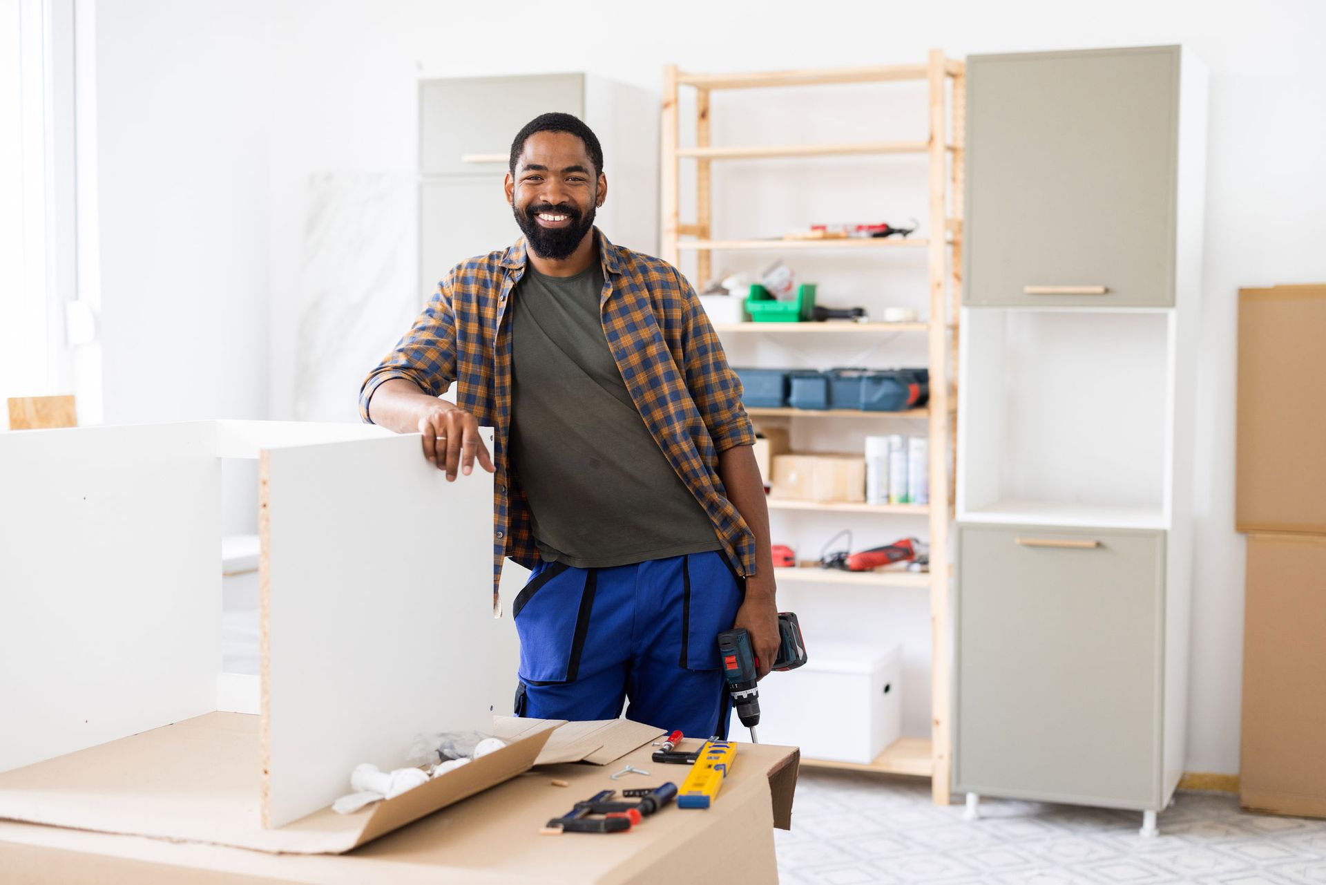 A professional handyman smiling confidently while holding a drill in his workshop.
