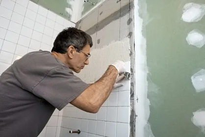 Person installing white tiles on a bathroom wall, using a trowel. Person installing white tiles on a bathroom wall, using a trowel.