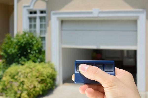 Hand holding blue remote, operating a partly open garage door. Hand holding blue remote, operating a partly open garage door.
