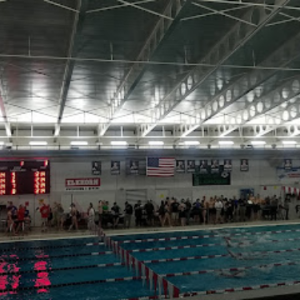 A group of people are standing around a large indoor swimming pool