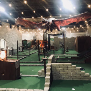 A dragon is hanging from the ceiling of an indoor golf course that has a castle theme.