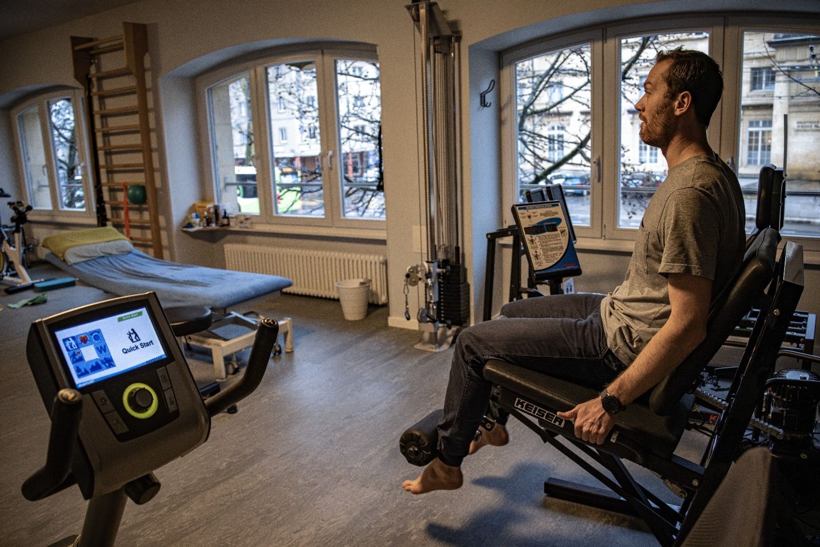 Un homme exerce ses jambes sur une machine d'extension des jambes assise dans une salle de sport, avec un vélo d'exercice visible au premier plan.