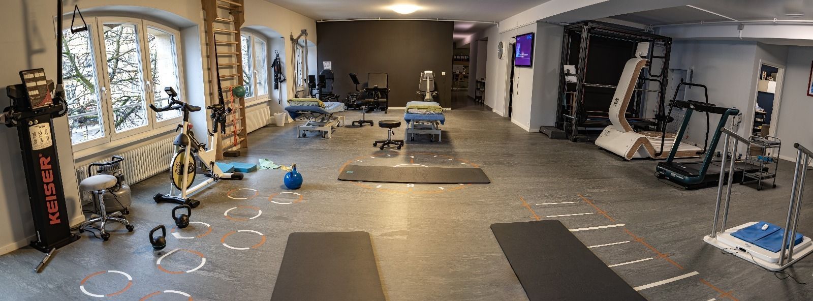Un centre de remise en forme avec divers équipements d'entraînement, notamment un vélo stationnaire, des poids, des tapis et des machines, disposés sur un sol gris.
