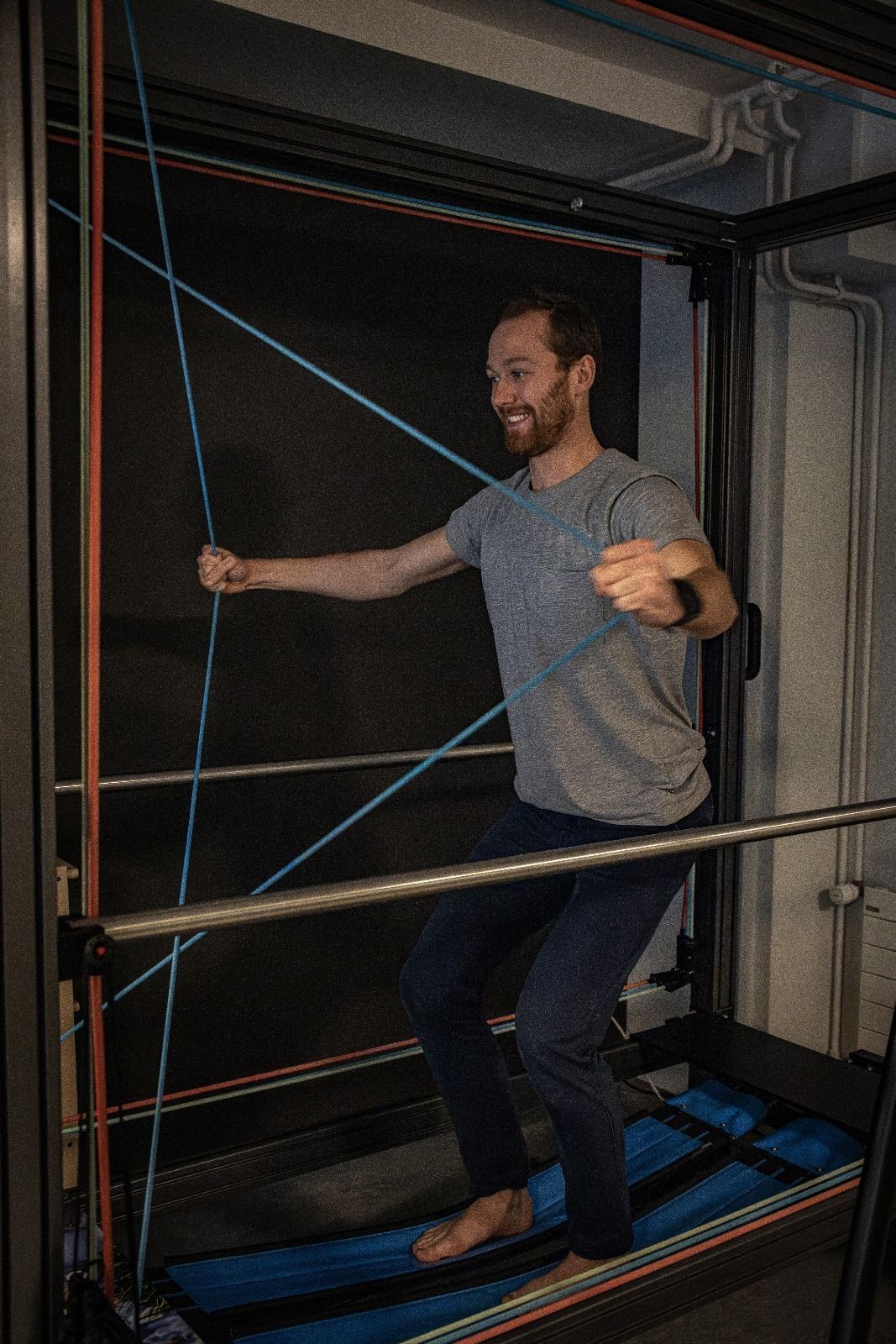 Un homme sourit en faisant de l'exercice sur une planche d'équilibre avec des bandes de résistance bleues et oranges et un fond noir.
