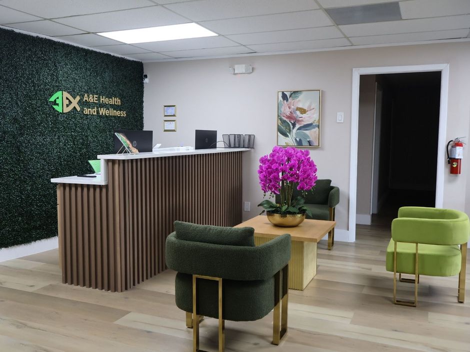 Modern reception area with wood desk, green chairs, purple flowers, and wall logo