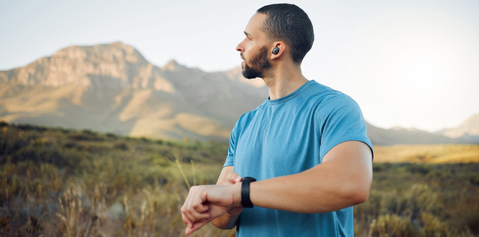 Man in a blue shirt checking his watch in a grassy field with mountains in the background