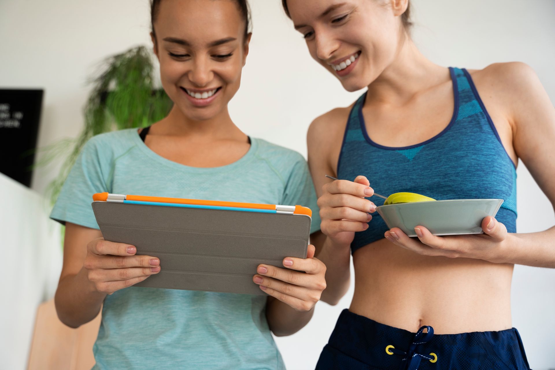 Two smiling people in workout clothes reviewing tablets together indoors