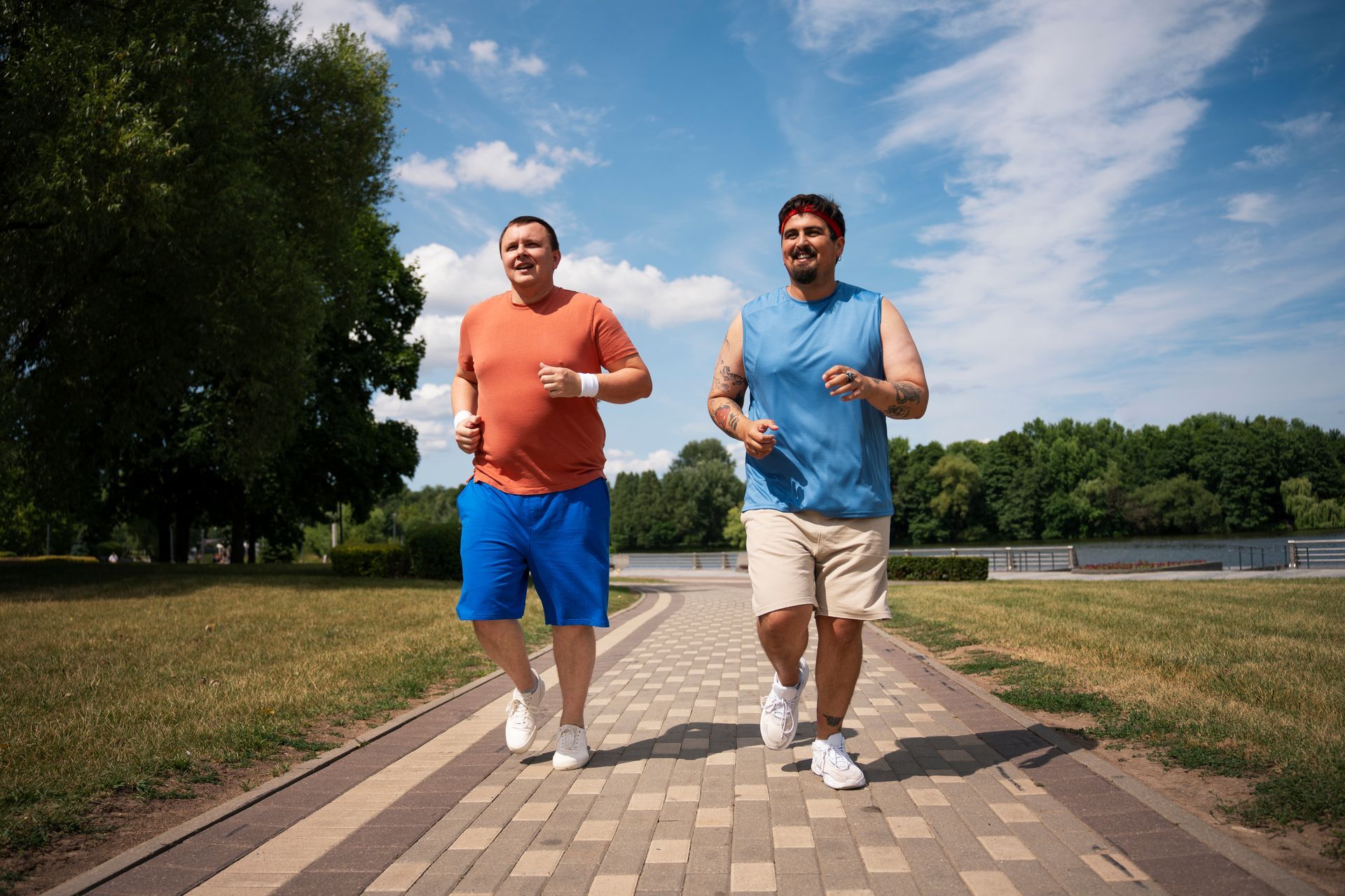 Two men jogging side by side on a park path, one in orange and blue, the other in blue and beige.