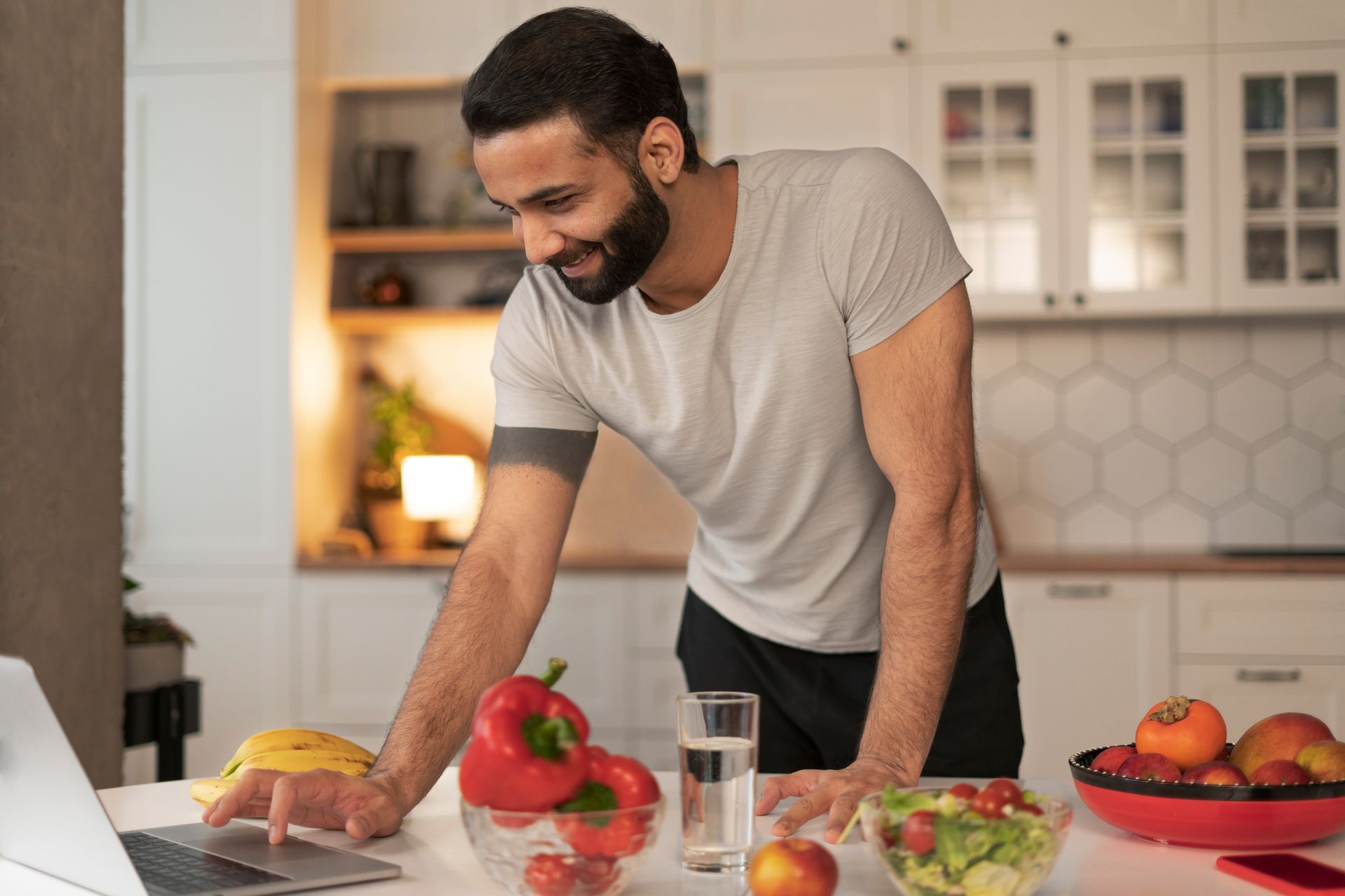 Man in a kitchen smiling while chopping fruit beside fresh produce on a counter