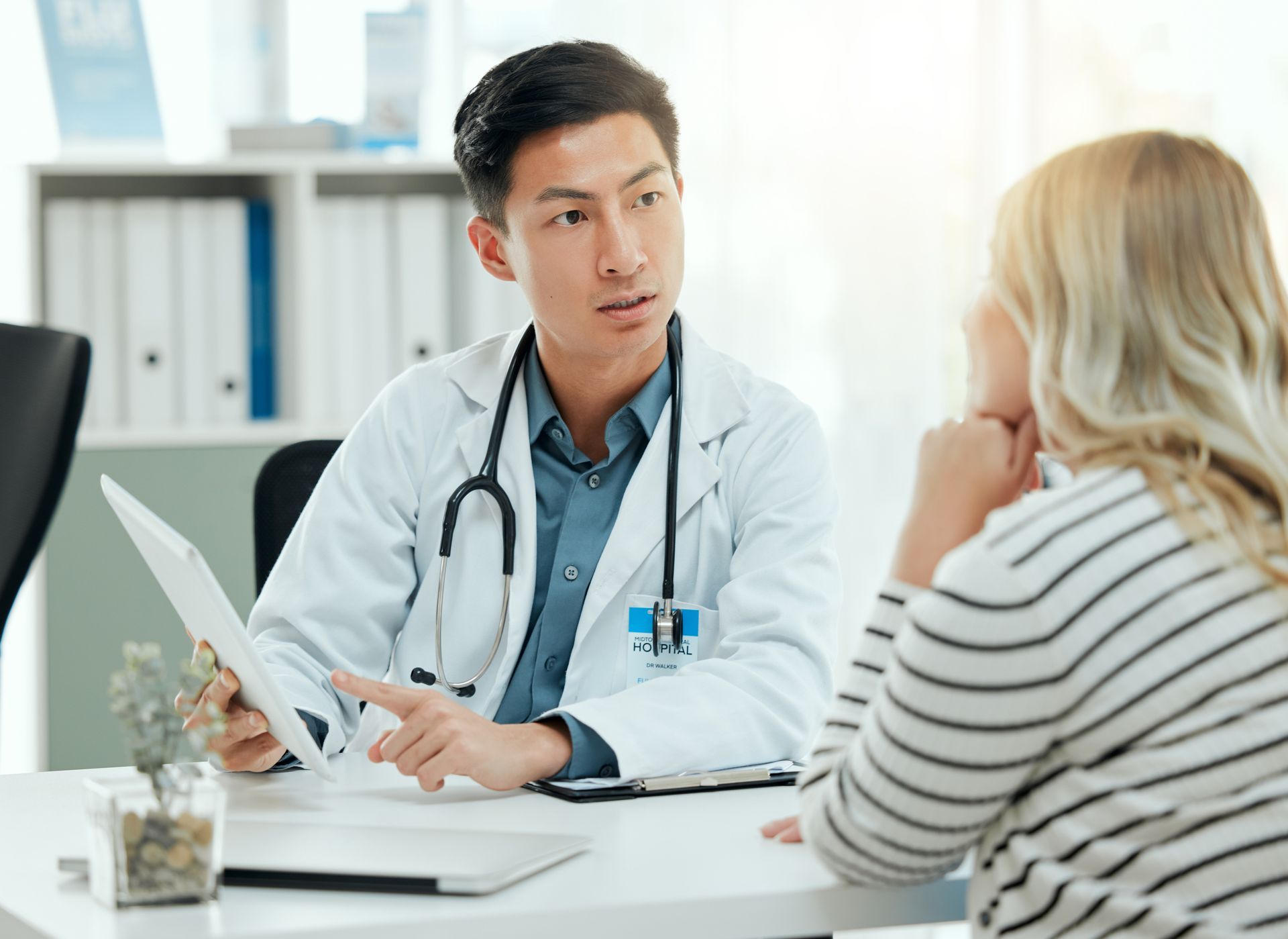 Doctor consulting with a patient at a desk in a bright clinic office, with a stethoscope and papers nearby