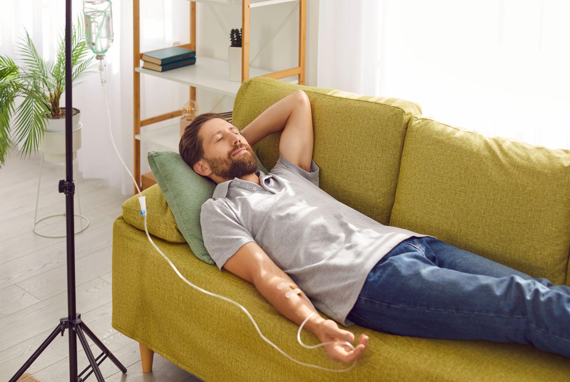 Man reclining on a yellow couch in a bright room, wearing headphones and holding a cable.