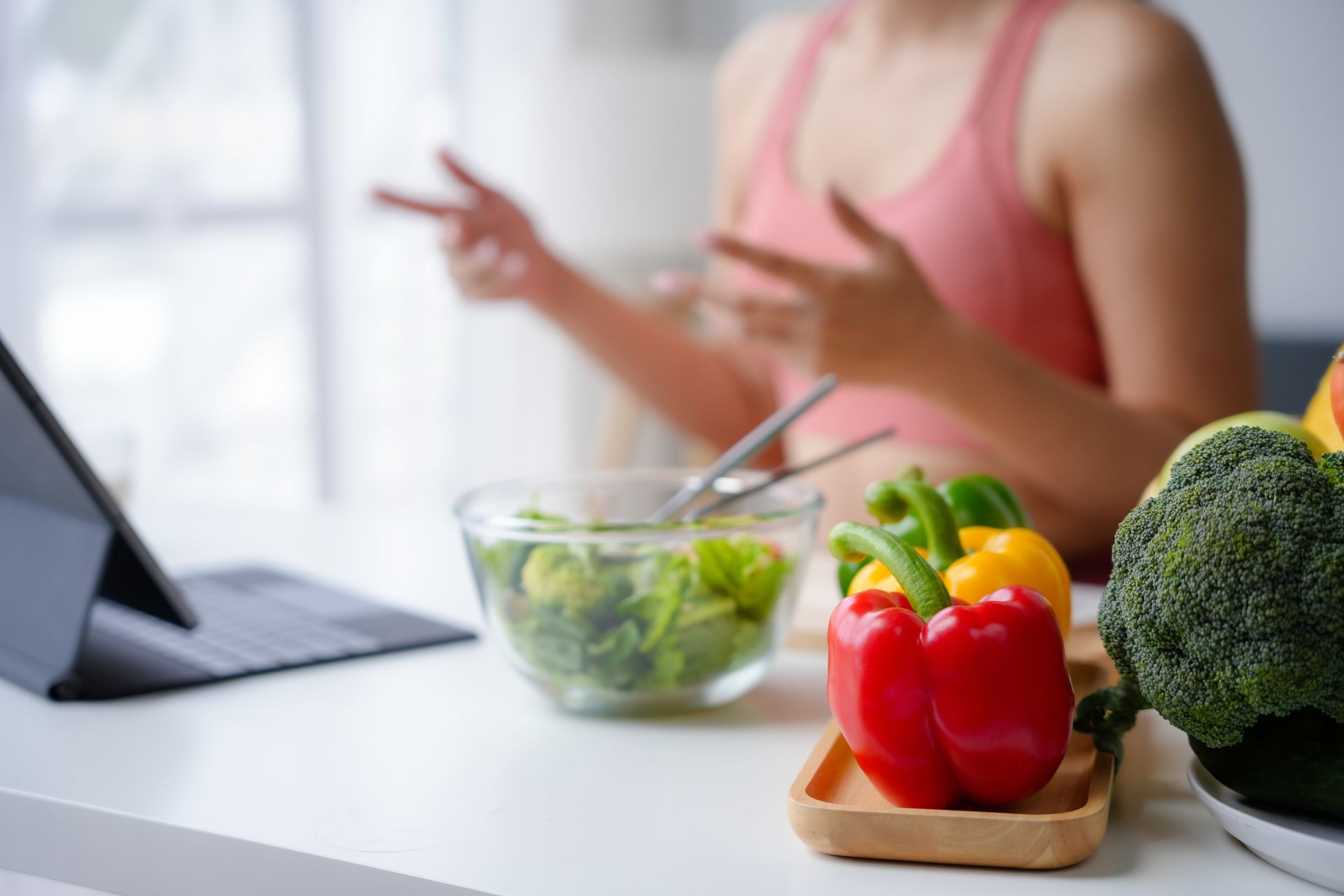 Healthy meal prep with vegetables on a kitchen counter and a person in the background using a tablet